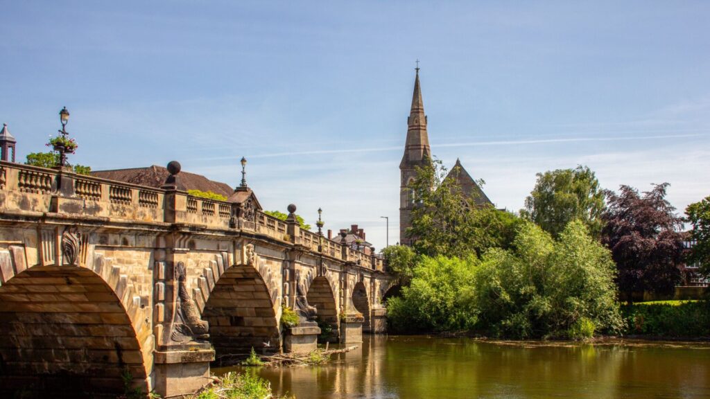 Charming view of Shrewsbury's stone bridge and church on a sunny summer day.